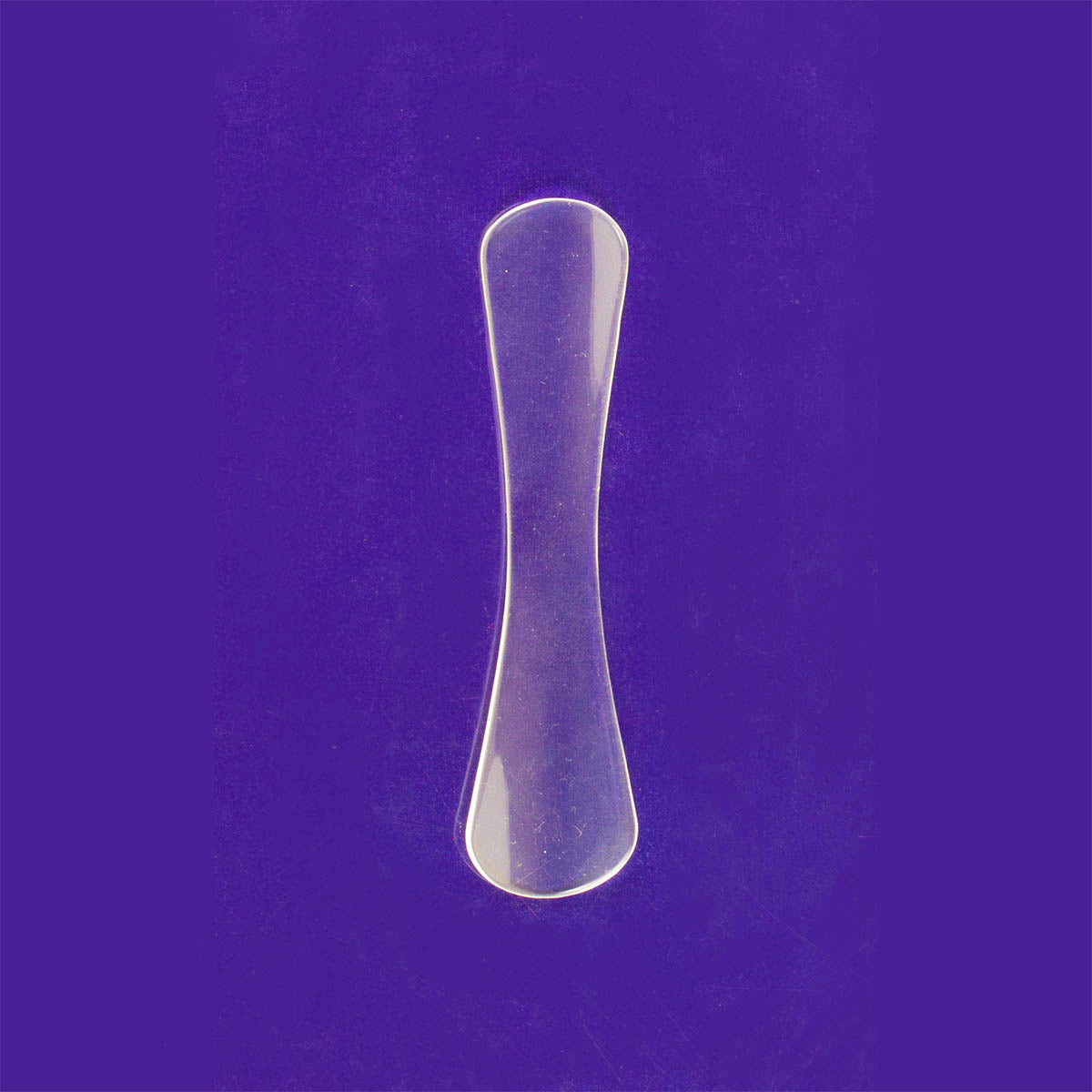 A clear plastic lid plate retractor against a purple background, typically used in ophthalmic surgery for eyelid procedures.